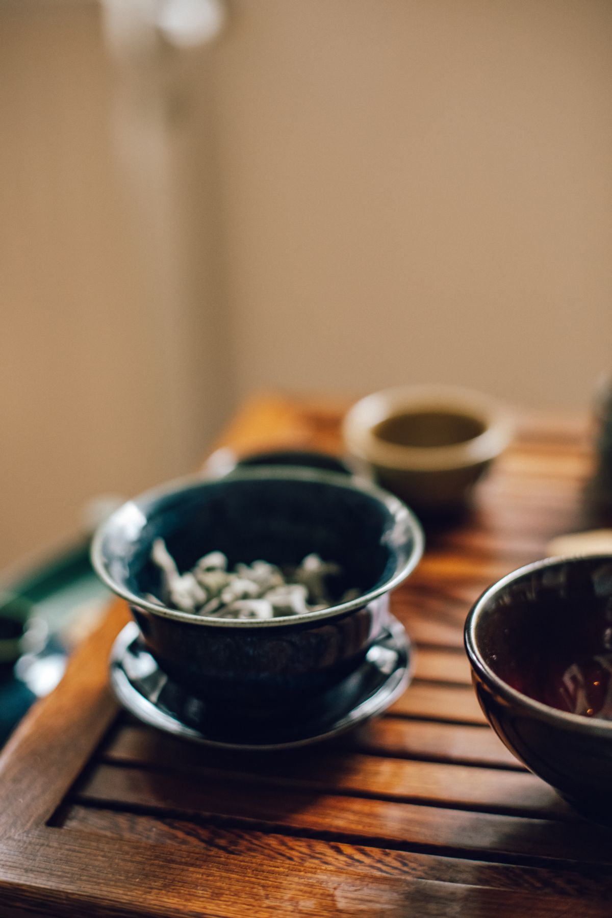 White tea leaves resting in a dark-glazed bowl on a wooden tea tray