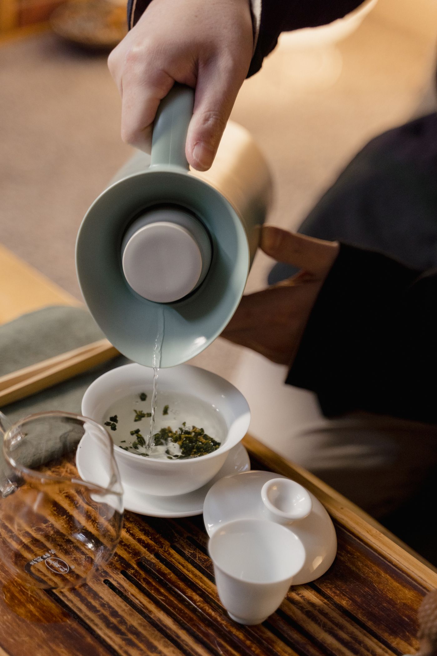 Hot water poured from a celadon kettle into a gaiwan of green tea leaves